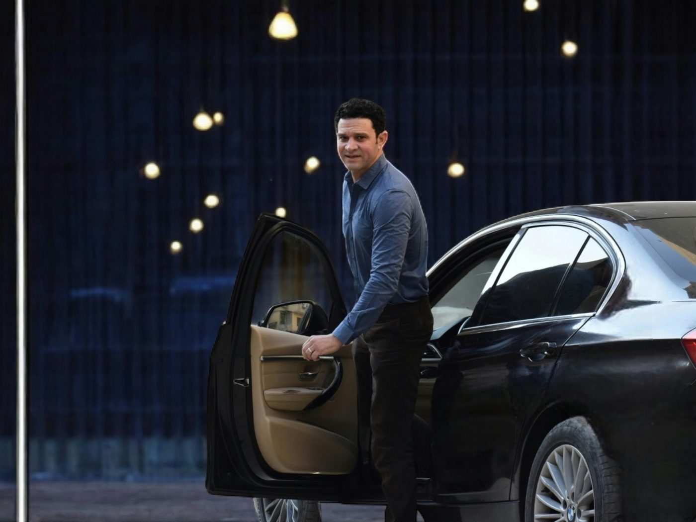 Man in a suit stepping out of a black executive car in the evening