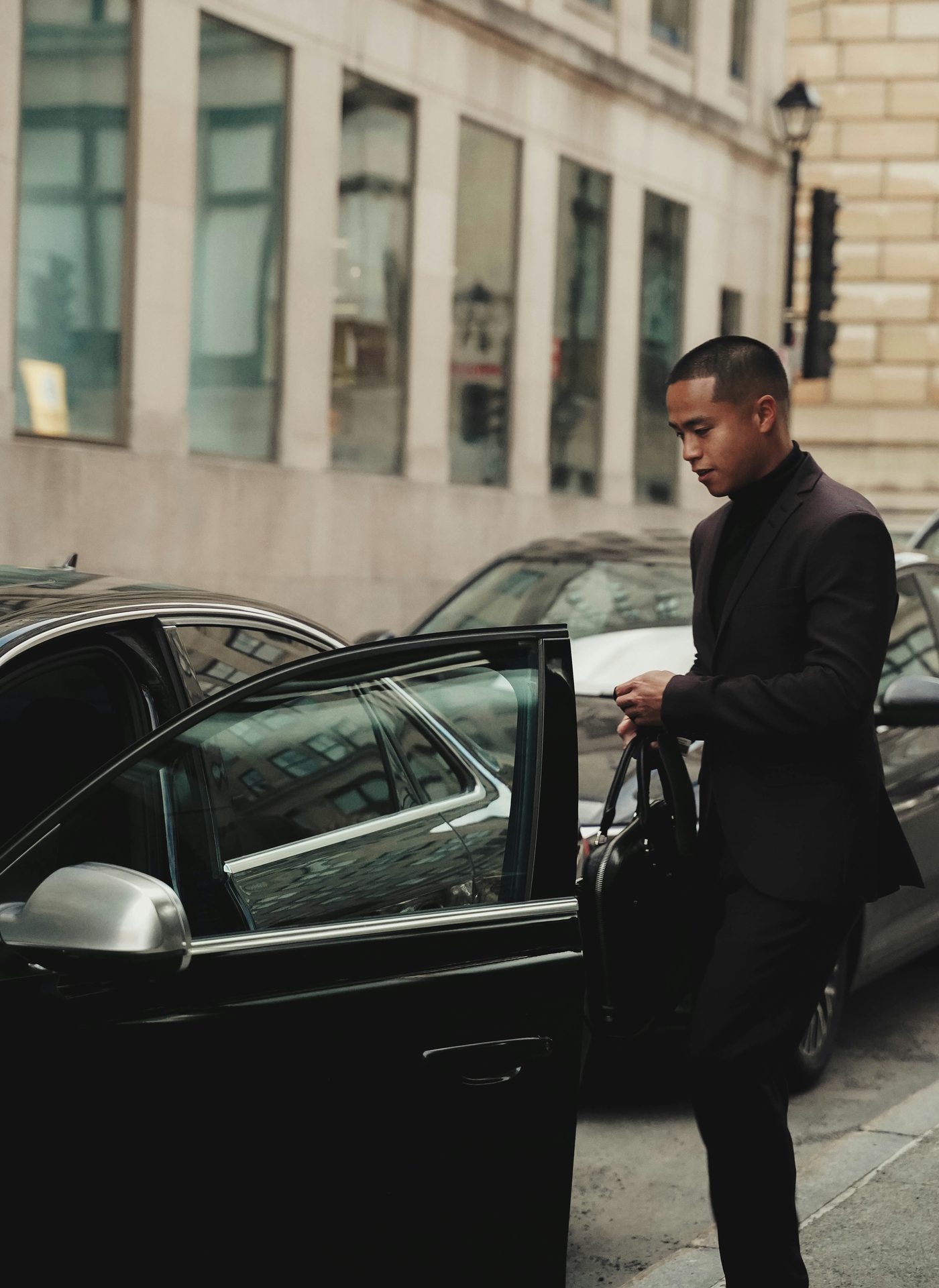 A chauffeur in a dark suit opening the door of a black car on a city street