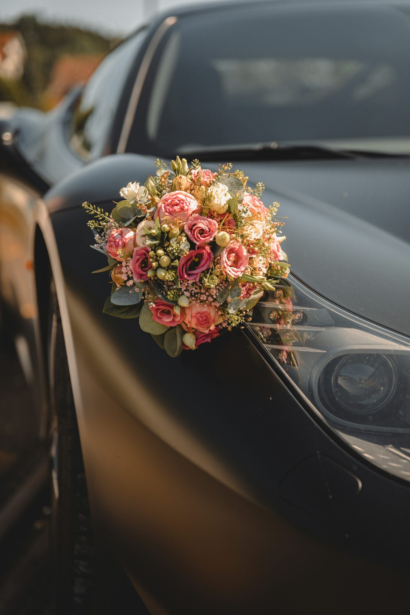Bouquet of flowers resting on the hood of a black wedding car