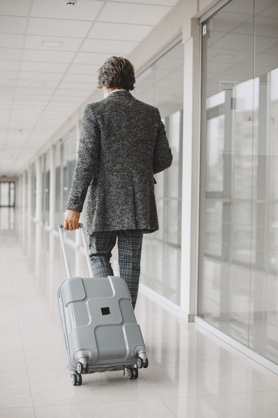 Businessman in a coat walking through an airport terminal with luggage